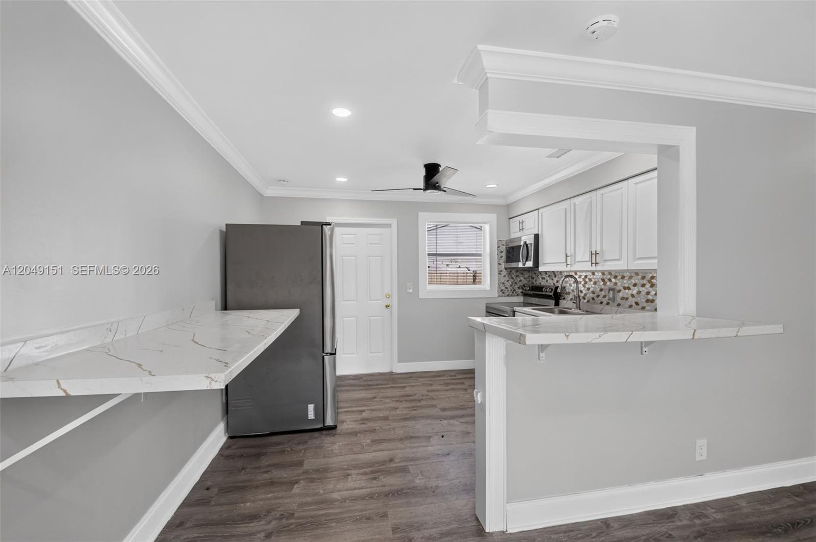 A kitchen features white cabinets, a marble-look breakfast bar, and dark wood-style flooring — 824 Bayberry Dr, Lake Park FL 33403, LAKE PARK, FL