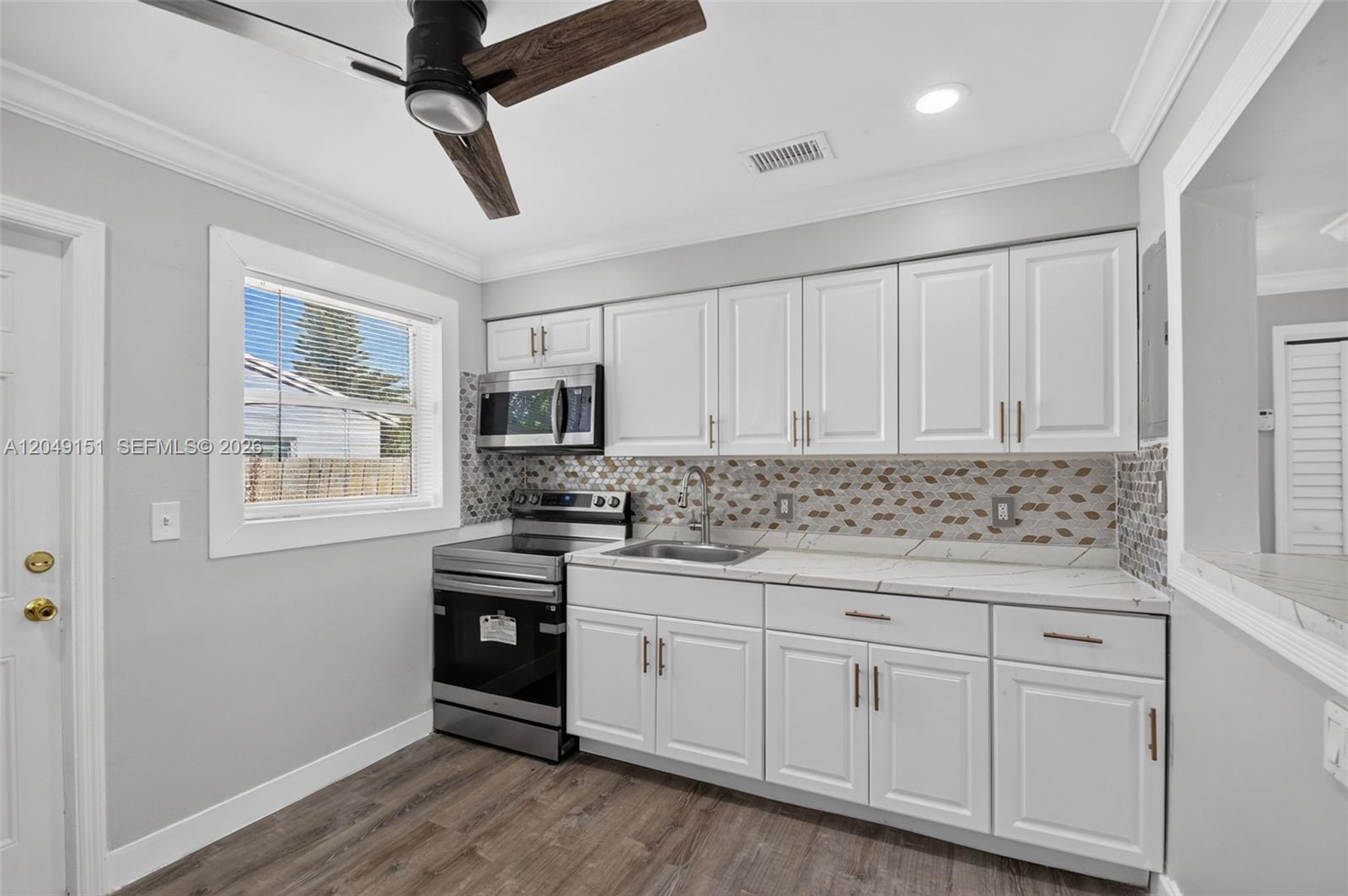 A kitchen features white cabinets, stainless steel appliances, a patterned backsplash, and wood-look flooring — 824 Bayberry Dr, Lake Park FL 33403, LAKE PARK, FL