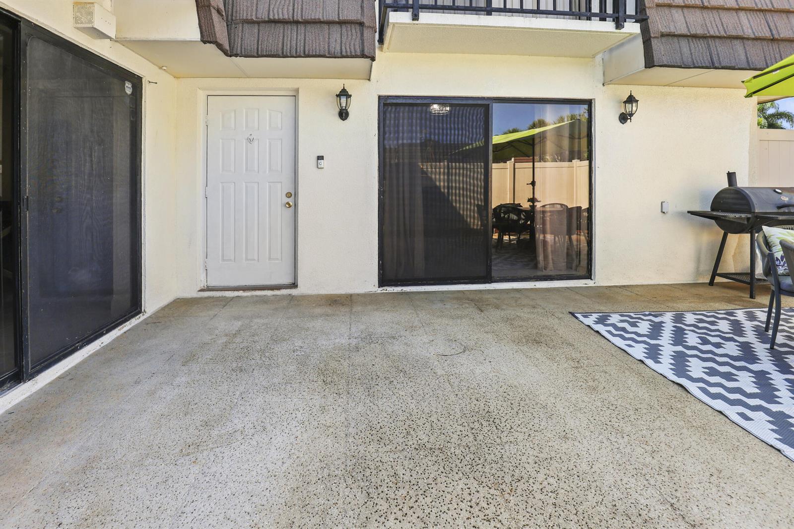 A concrete patio features a white door, sliding glass doors, and a charcoal grill — 7813 78th Way, West Palm Beach FL 33407, WEST PALM BEACH, FL