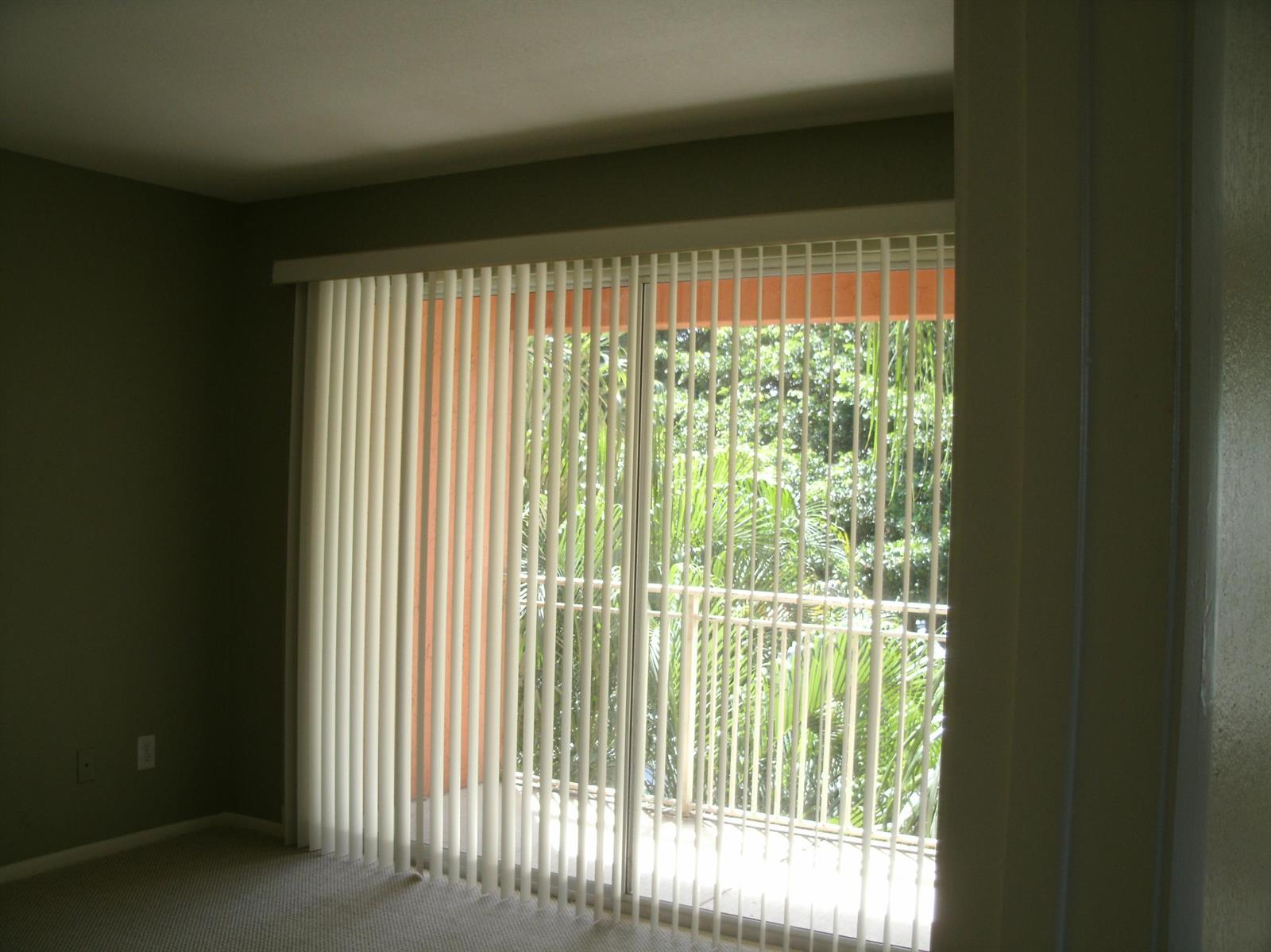 A room with beige carpet and vertical blinds covering a sliding glass door to a balcony — 1780 Palm Cove Boulevard # 302, Delray Beach FL 33445, DELRAY BEACH, FL