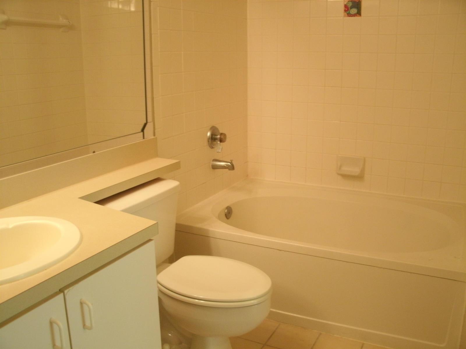 A bathroom features a white vanity, a toilet, and a tiled tub-shower combination — 1780 Palm Cove Boulevard # 302, Delray Beach FL 33445, DELRAY BEACH, FL