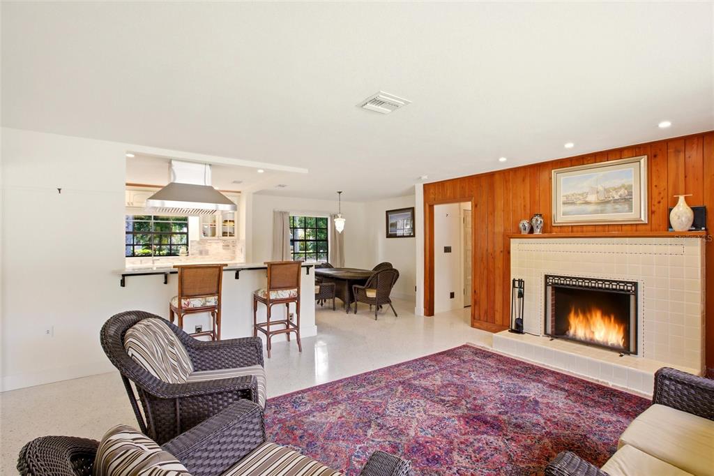 A living room with a fireplace, wood-paneled wall, and an open kitchen with bar seating — 2706 RHODE ISLAND AVENUE, FORT MYERS, FL