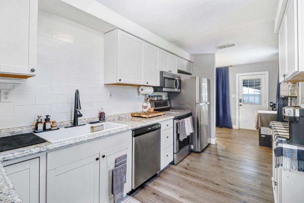 A kitchen features white cabinets, a farmhouse sink, stainless steel appliances, and light-colored countertops — 11110 HACKNEY DRIVE, RIVERVIEW, FL
