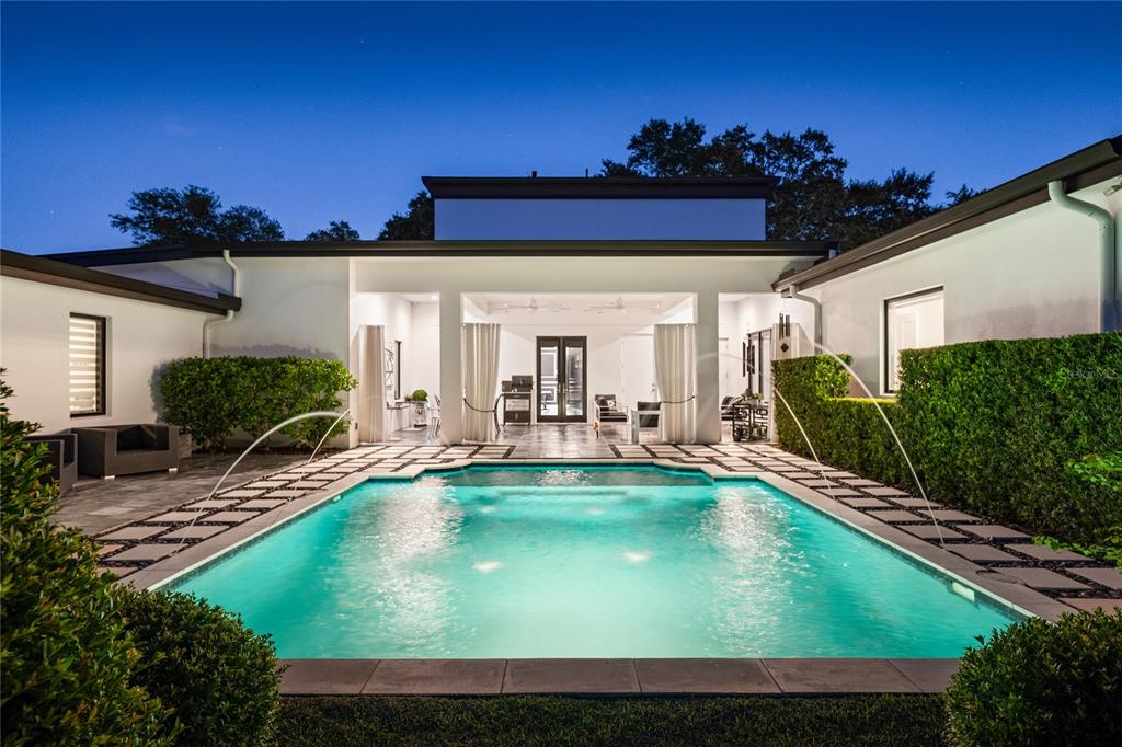 A rectangular swimming pool with fountains sits in the courtyard of a modern white house — 1581 FOREST AVENUE, WINTER PARK, FL