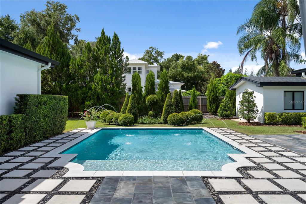 A rectangular swimming pool with fountains sits between two white buildings in a landscaped backyard — 1581 FOREST AVENUE, WINTER PARK, FL