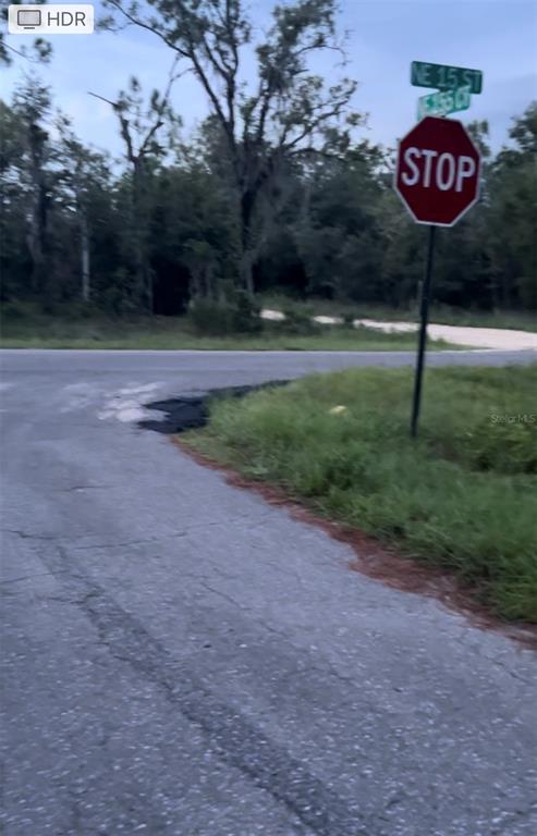 A stop sign stands at a rural intersection with a paved road and wooded background — Lot 20 NE 155TH COURT, WILLISTON, FL
