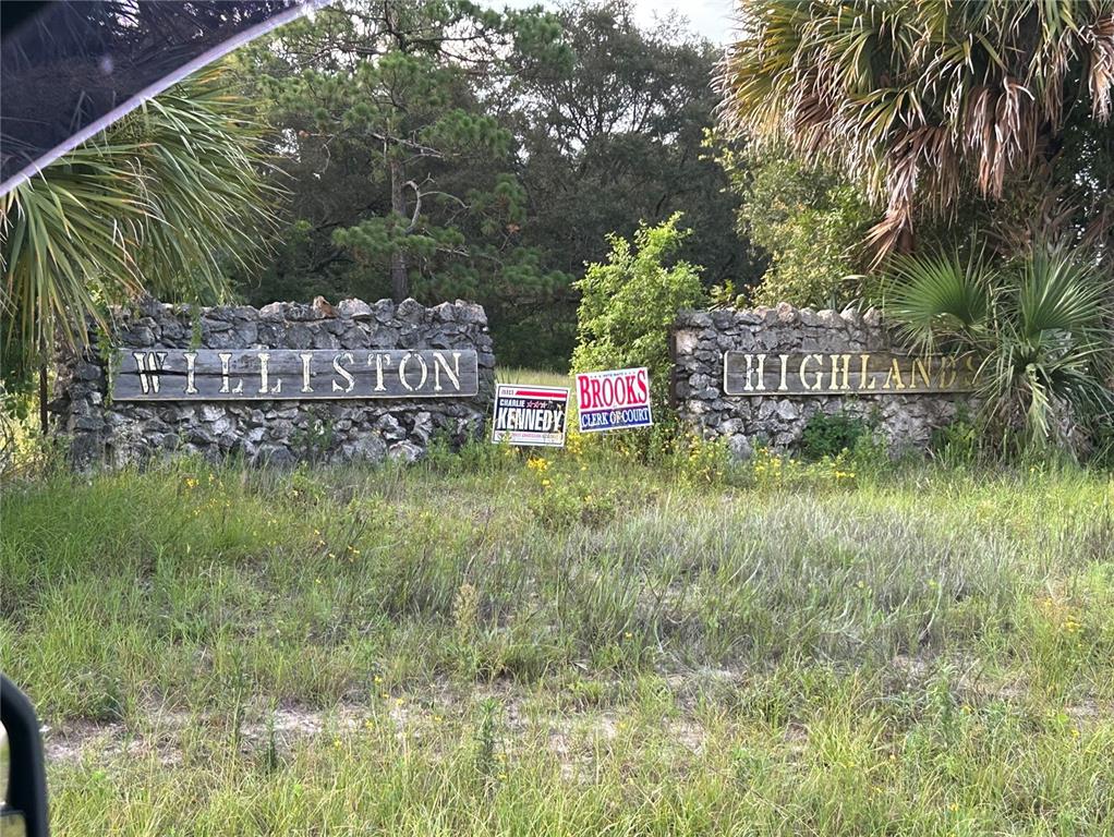 A stone entrance sign for Williston Highlands stands in a grassy field with political signs — Lot 20 NE 155TH COURT, WILLISTON, FL
