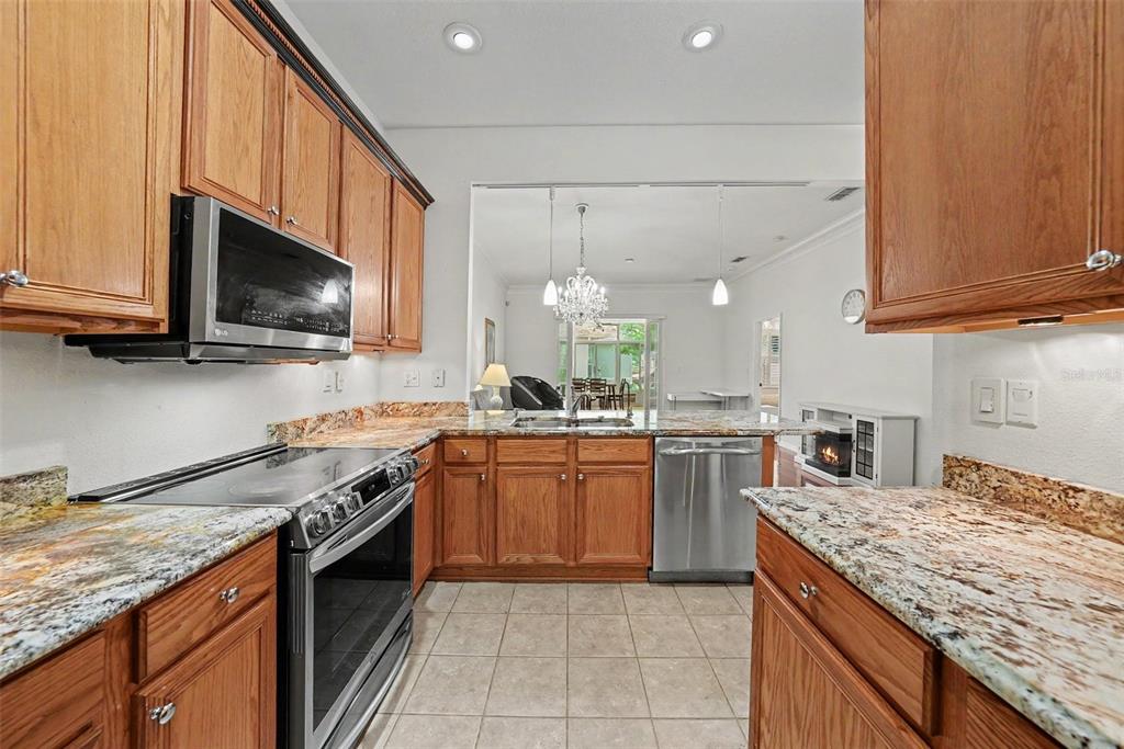 A kitchen features wood cabinets, granite countertops, stainless steel appliances, and tile flooring — 7411 WIMPOLE DRIVE, NEW PORT RICHEY, FL