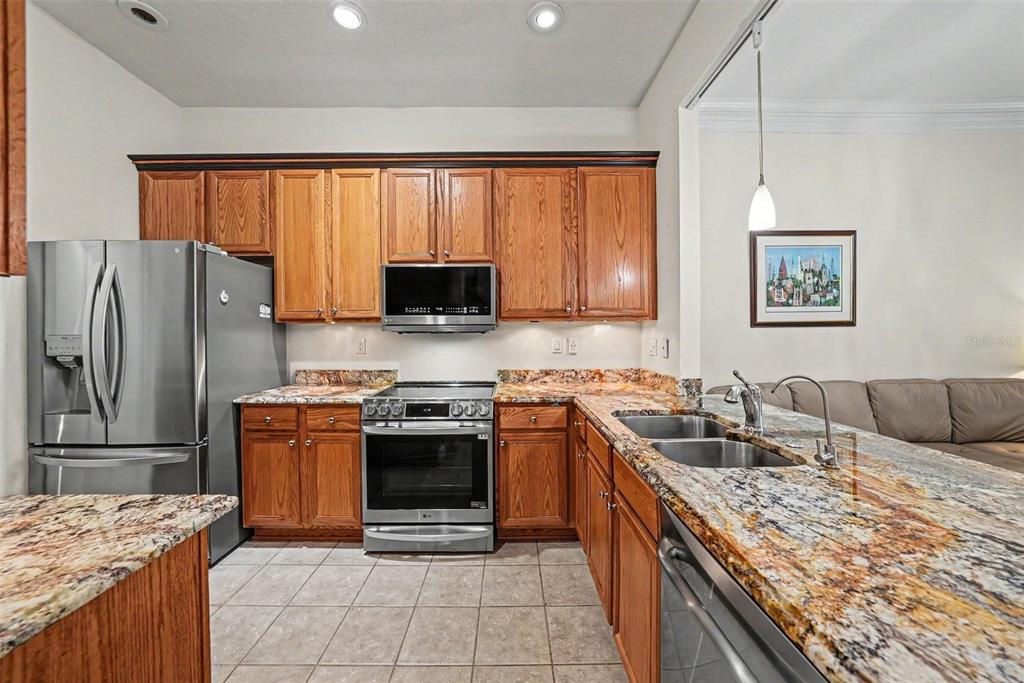 A kitchen with wood cabinets, granite countertops, stainless steel appliances, and tile flooring — 7411 WIMPOLE DRIVE, NEW PORT RICHEY, FL