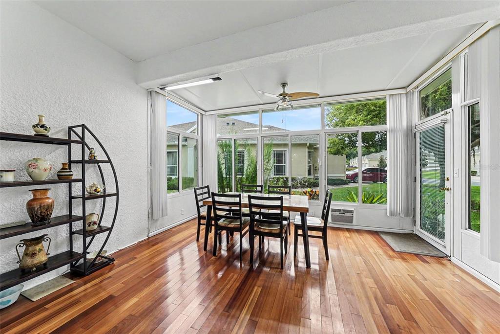 A sunroom features hardwood floors, a dining set, and large windows overlooking a neighborhood — 7411 WIMPOLE DRIVE, NEW PORT RICHEY, FL