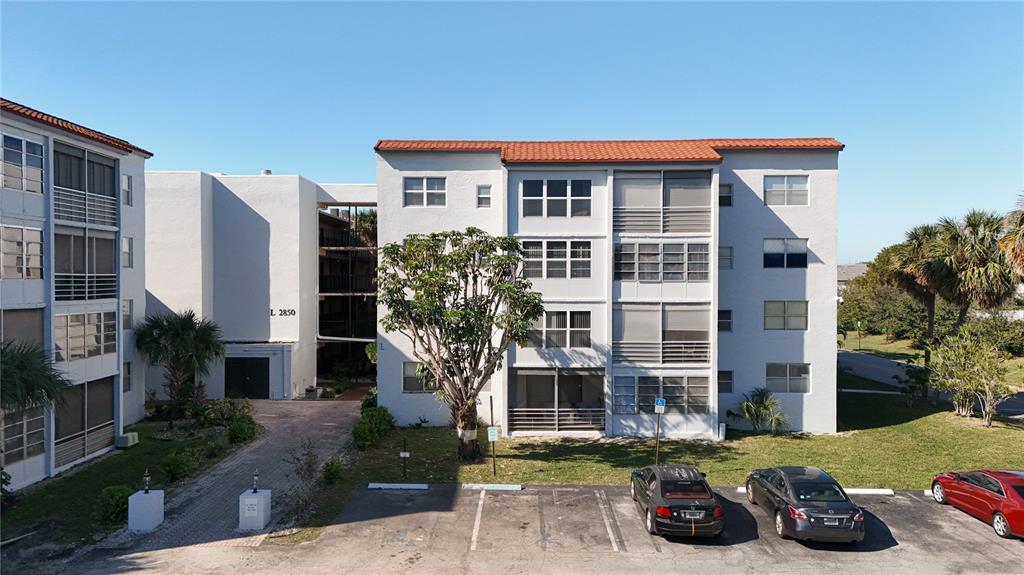 An exterior view of a multi-story apartment building with a parking lot in front — 2850 SOMERSET DRIVE UNIT 204L, LAUDERDALE LAKES, FL