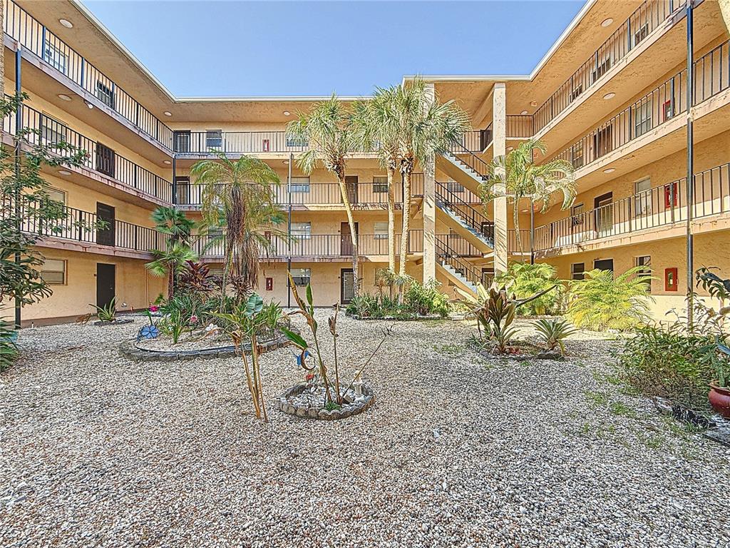 An exterior view of a multi-story apartment building courtyard with gravel landscaping and palm trees — 2850 SOMERSET DRIVE UNIT 204L, LAUDERDALE LAKES, FL