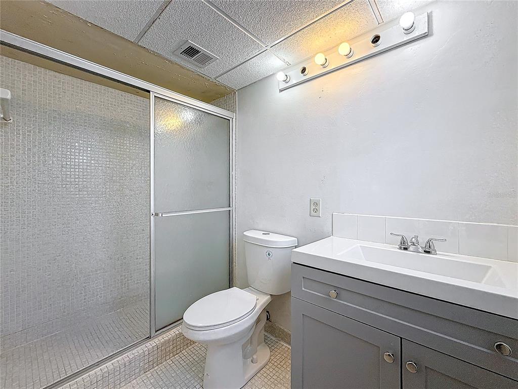 A bathroom features a gray vanity, a white toilet, and a walk-in tiled shower — 2850 SOMERSET DRIVE UNIT 204L, LAUDERDALE LAKES, FL