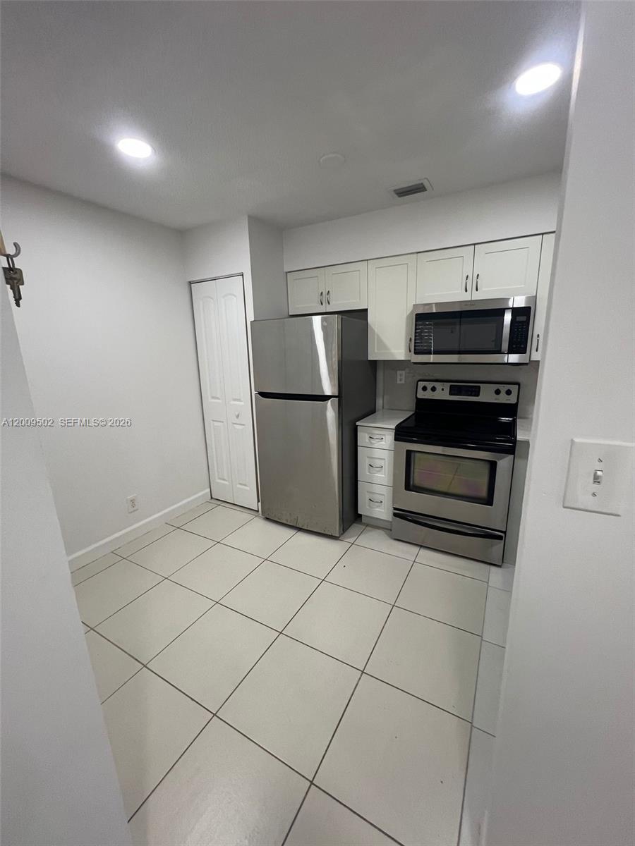 A kitchen features white cabinets, stainless steel appliances, and light-colored floor tiles — 9203 SW 138th Pl # 9203, Miami FL 33186, MIAMI, FL