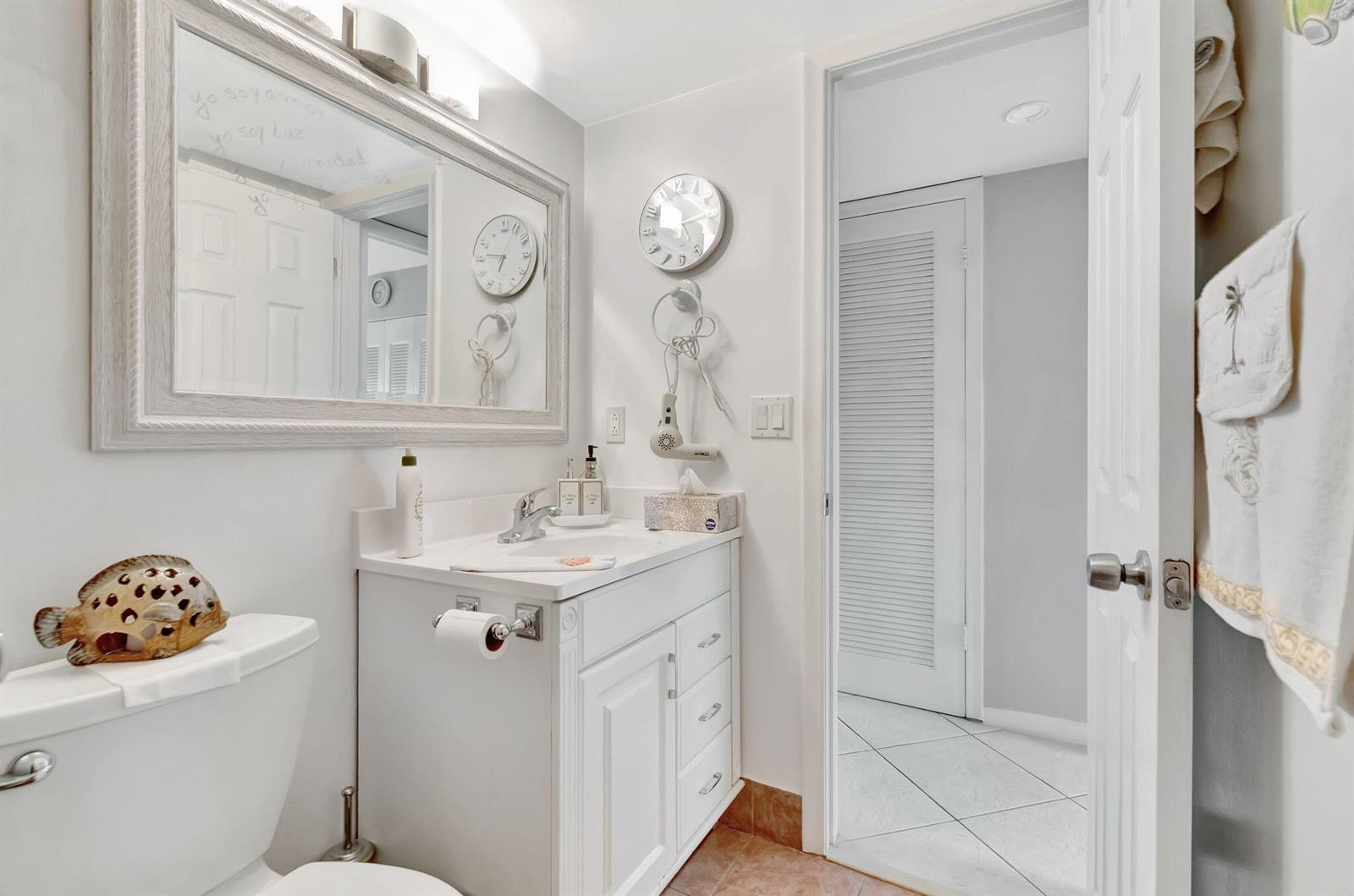 A bathroom features a white vanity, a large mirror, a toilet, and a doorway — 46 Andover B, West Palm Beach FL 33417, WEST PALM BEACH, FL
