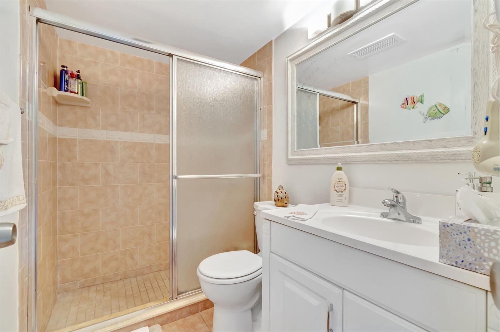 A bathroom features a tiled walk-in shower, a white vanity, and a toilet — 46 Andover B, West Palm Beach FL 33417, WEST PALM BEACH, FL