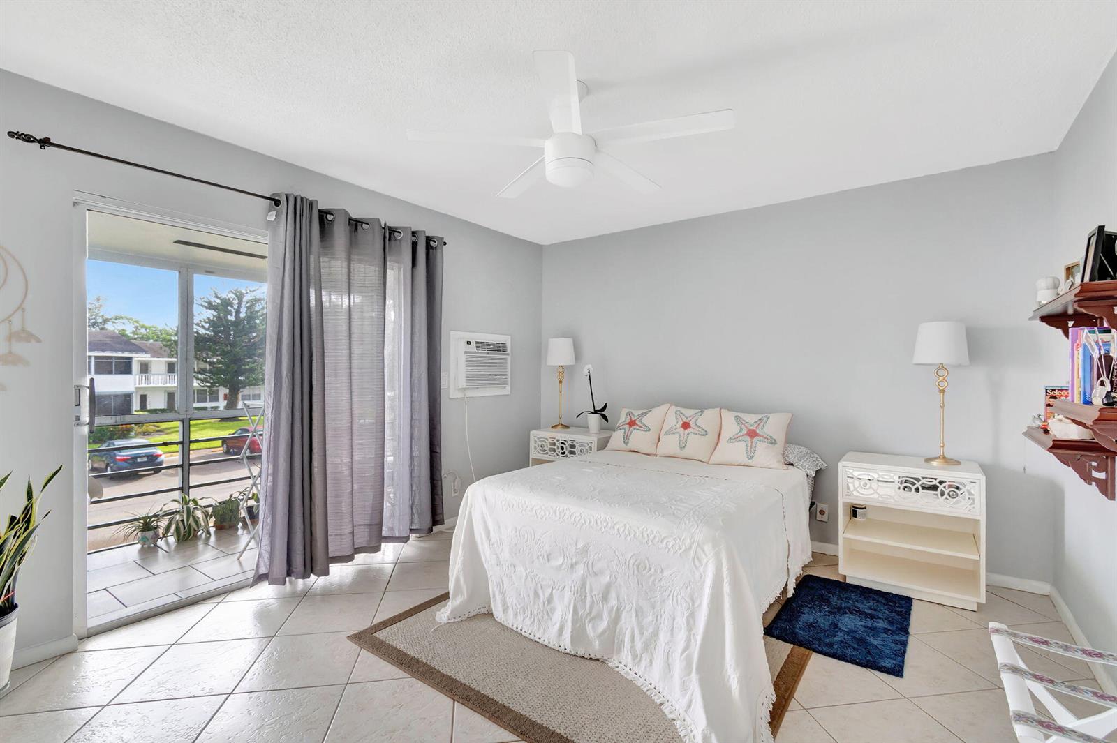 A bedroom features a bed with starfish pillows, tile flooring, and a sliding glass door — 46 Andover B, West Palm Beach FL 33417, WEST PALM BEACH, FL