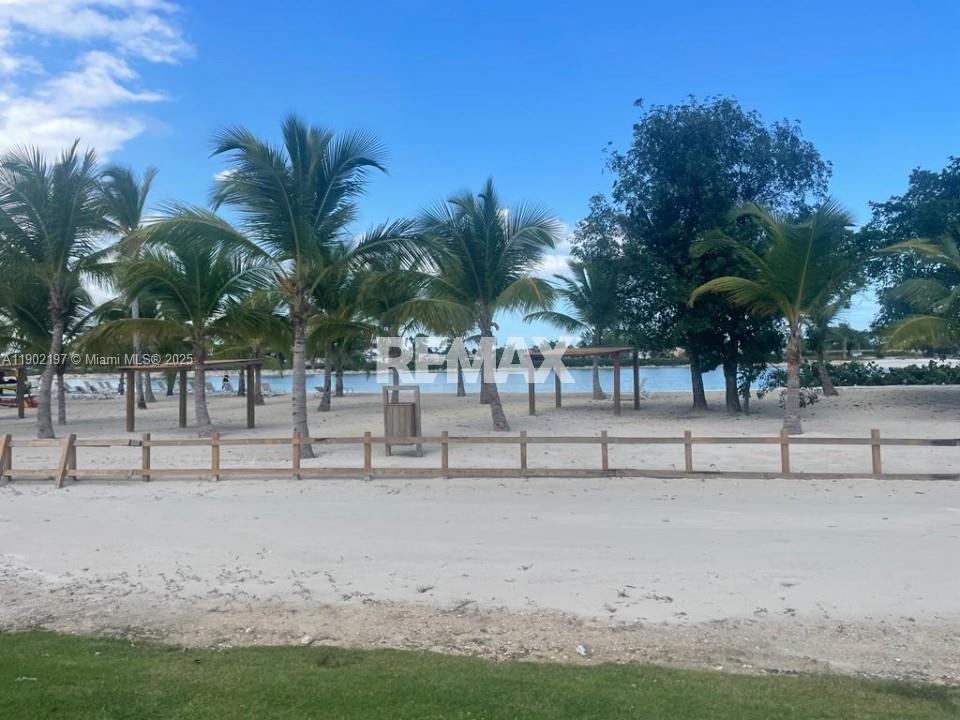 A sandy beach area features palm trees, wooden structures, and a low fence — Vista cana punta cana, PU 2300, PU
