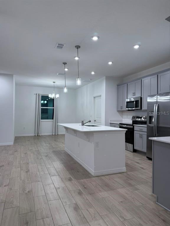 A kitchen features a white island, gray cabinetry, stainless steel appliances, and light wood-look flooring — 6518 WATERLILY PLACE, LAKE HAMILTON, FL