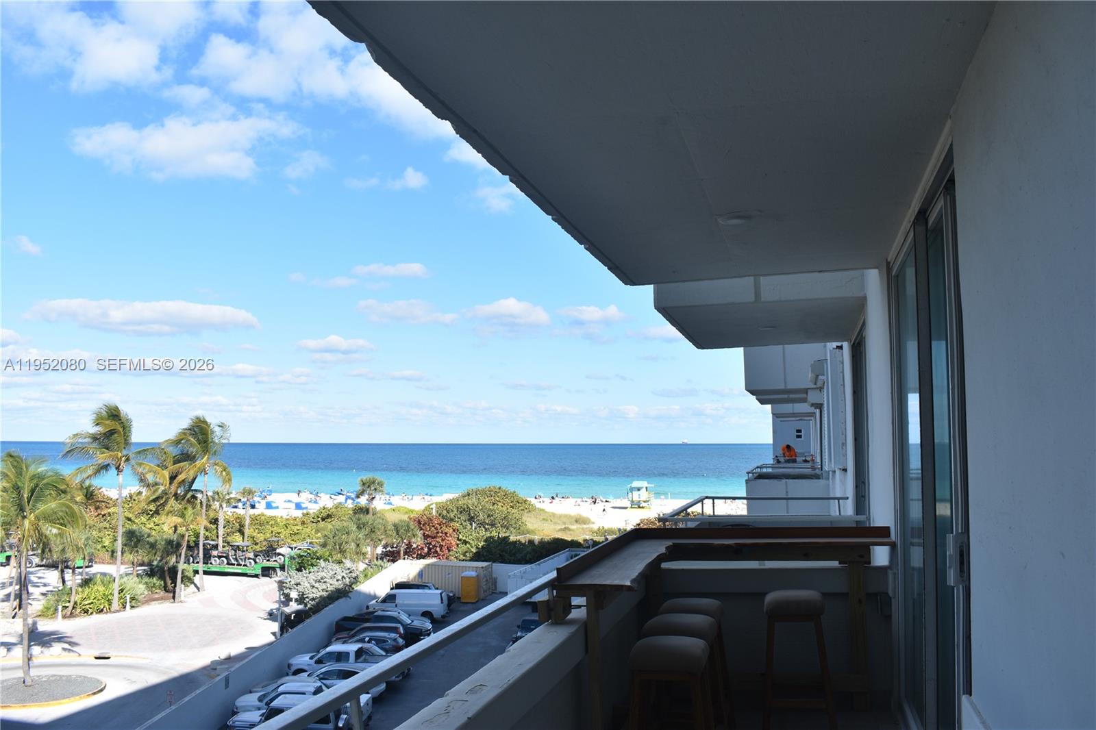 A balcony with a wooden bar and stools overlooks a beach and parking lot — 465 Ocean Dr # 524, Miami Beach FL 33139, MIAMI BEACH, FL