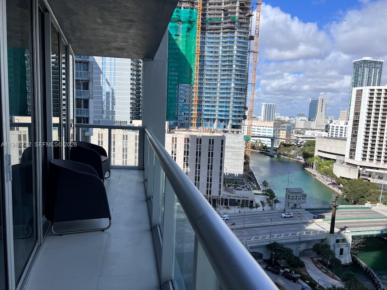 A balcony with two chairs overlooks a river, a bridge, and surrounding city high-rises — 475 Brickell Ave # 1715, Miami FL 33131, MIAMI, FL
