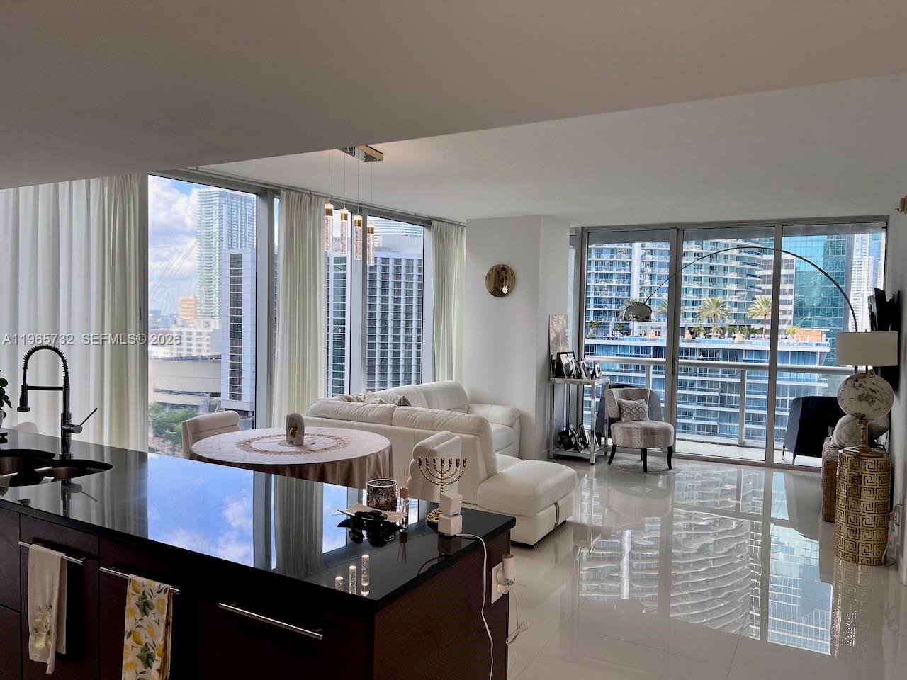 A modern open-concept living area features a dark kitchen island, white sofa, and floor-to-ceiling windows — 475 Brickell Ave # 1715, Miami FL 33131, MIAMI, FL