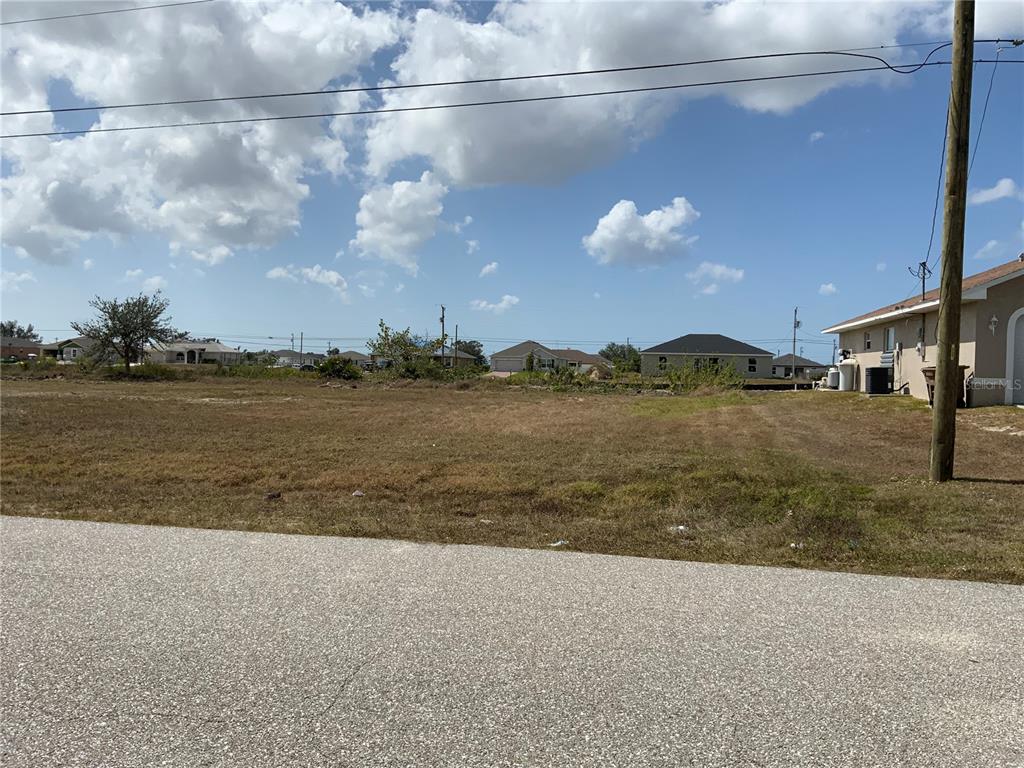 A vacant, grassy residential lot sits alongside a paved road with houses in the background — 1708 NW 6TH PLACE, CAPE CORAL, FL