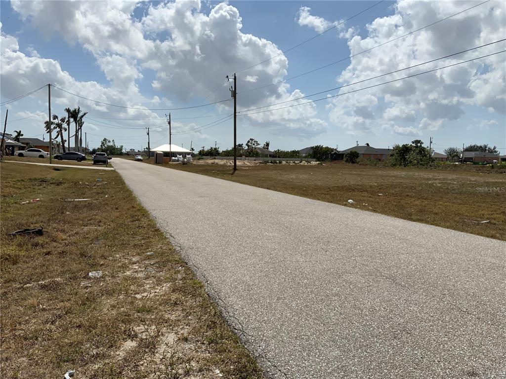 A paved road runs through a vacant residential lot under a cloudy sky — 1708 NW 6TH PLACE, CAPE CORAL, FL