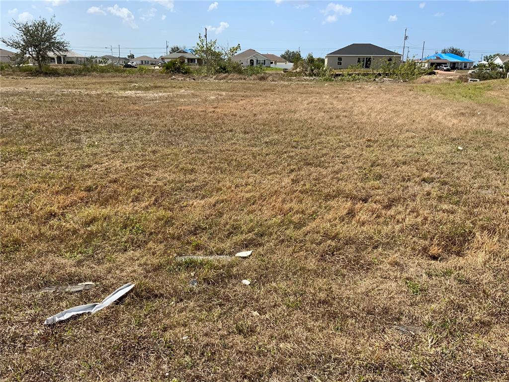 A vacant, grassy lot with scattered debris and residential houses in the background — 1708 NW 6TH PLACE, CAPE CORAL, FL