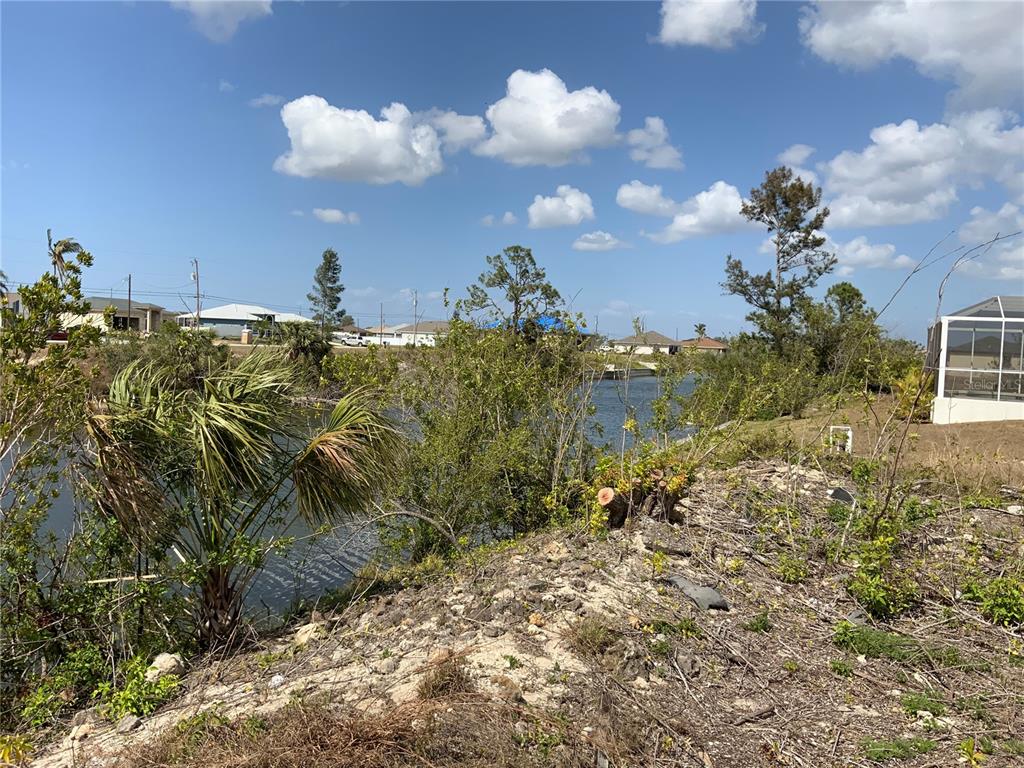 A view of a canal from a grassy, undeveloped waterfront lot under a blue sky — 1708 NW 6TH PLACE, CAPE CORAL, FL