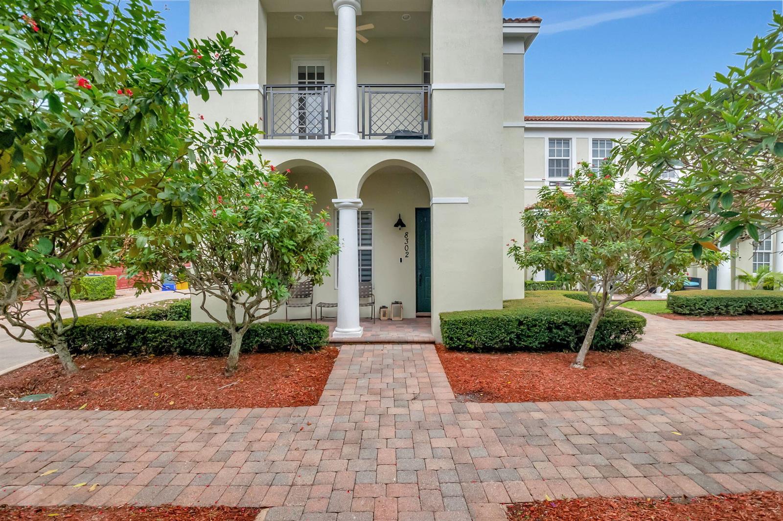 A two-story townhouse exterior features a paved walkway, arched entryway, and a second-floor balcony — 8302 NW 8th Terrace # 8302, Boca Raton FL 33487, BOCA RATON, FL