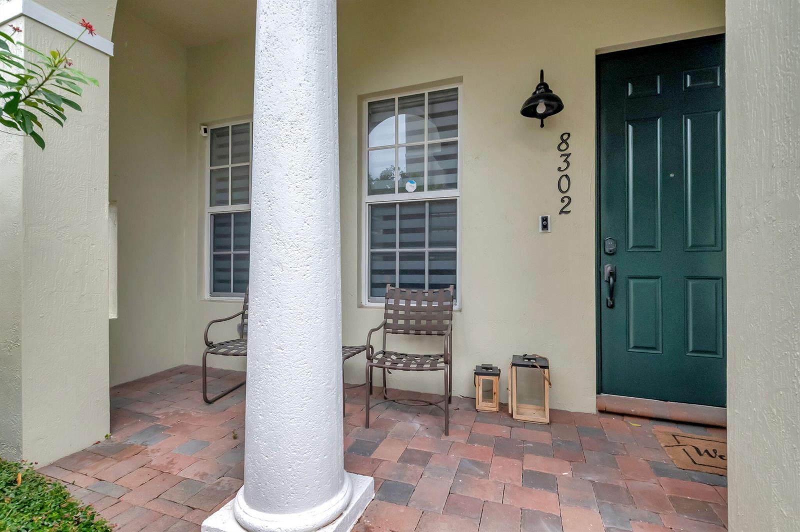 A covered front porch features brick pavers, a white column, two chairs, and a green door — 8302 NW 8th Terrace # 8302, Boca Raton FL 33487, BOCA RATON, FL