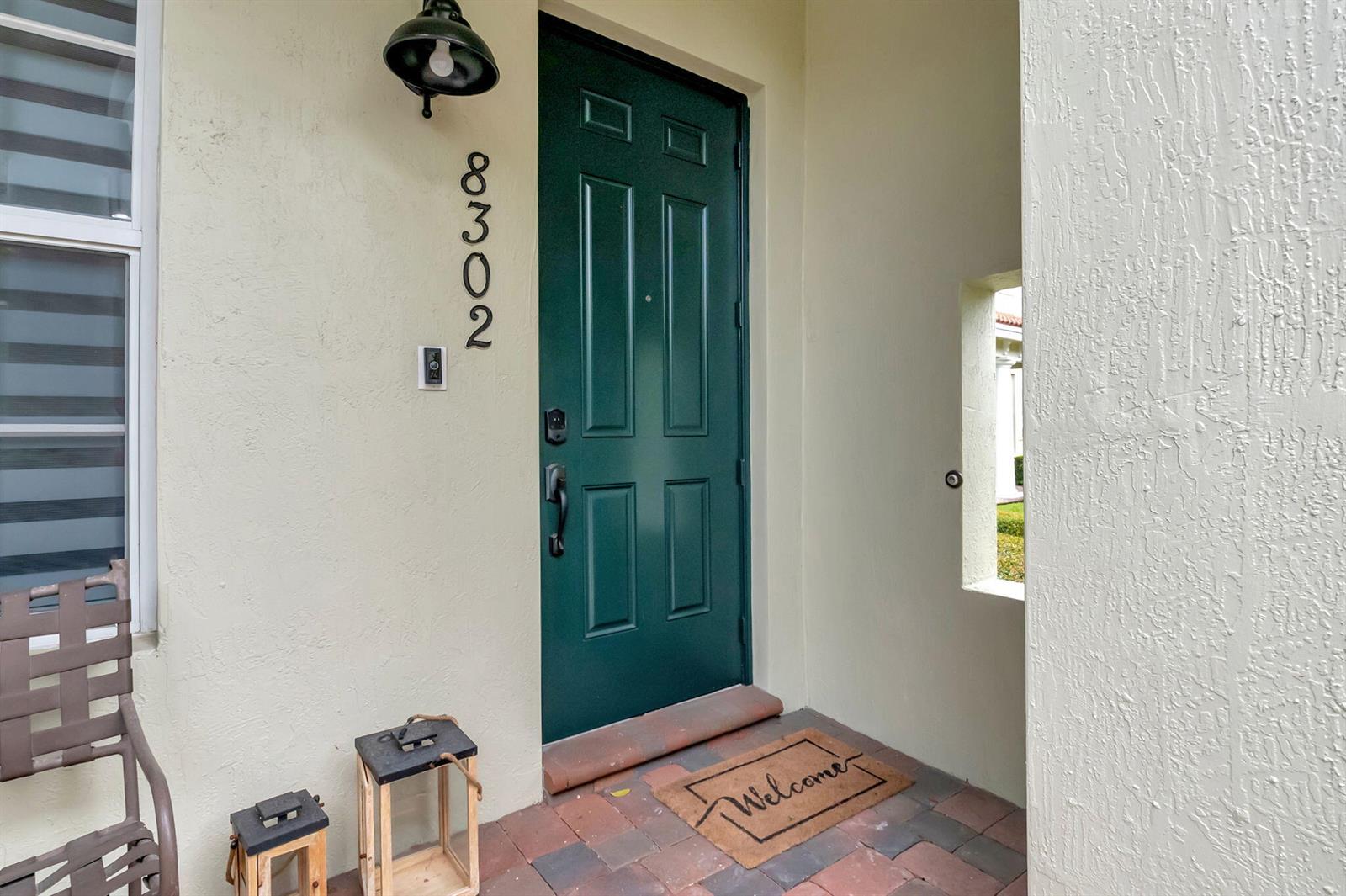 A green front door with a welcome mat sits on a paved porch — 8302 NW 8th Terrace # 8302, Boca Raton FL 33487, BOCA RATON, FL
