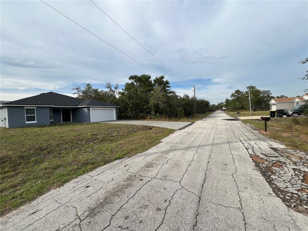 A gray single-story house with a white garage sits beside a cracked asphalt road — 1205 ALAFIA WAY, KISSIMMEE, FL