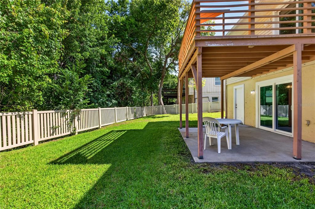 A backyard features a concrete patio, a white plastic table and chair, and a wooden deck — 51 SANDPIPER CIRCLE, ORMOND BEACH, FL