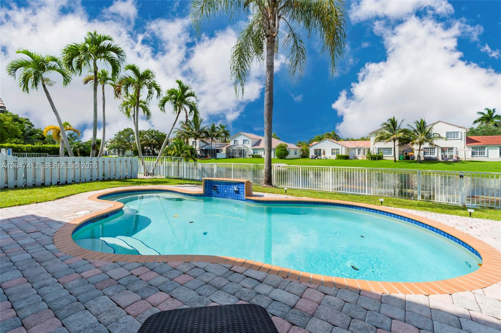 A backyard swimming pool with a water feature overlooks a lake and neighboring houses — 18785 SW 29th St, Miramar FL 33029, MIRAMAR, FL