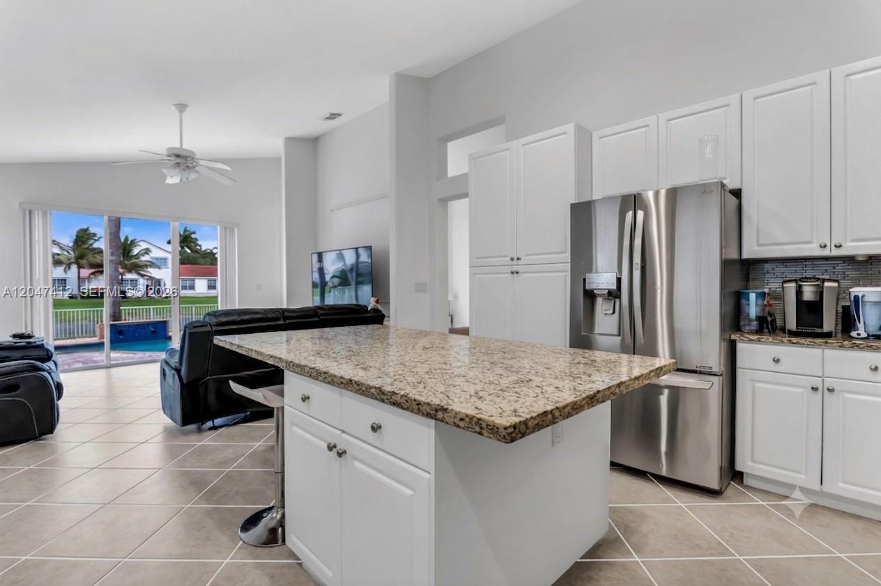 A kitchen with a granite island, white cabinets, and stainless steel appliances overlooks a living area — 18785 SW 29th St, Miramar FL 33029, MIRAMAR, FL