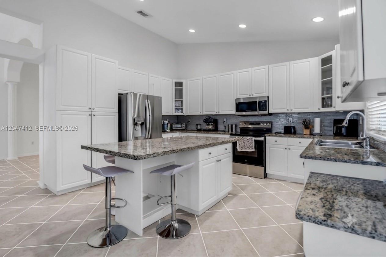 A kitchen features white cabinets, granite countertops, a center island with stools, and tile flooring — 18785 SW 29th St, Miramar FL 33029, MIRAMAR, FL
