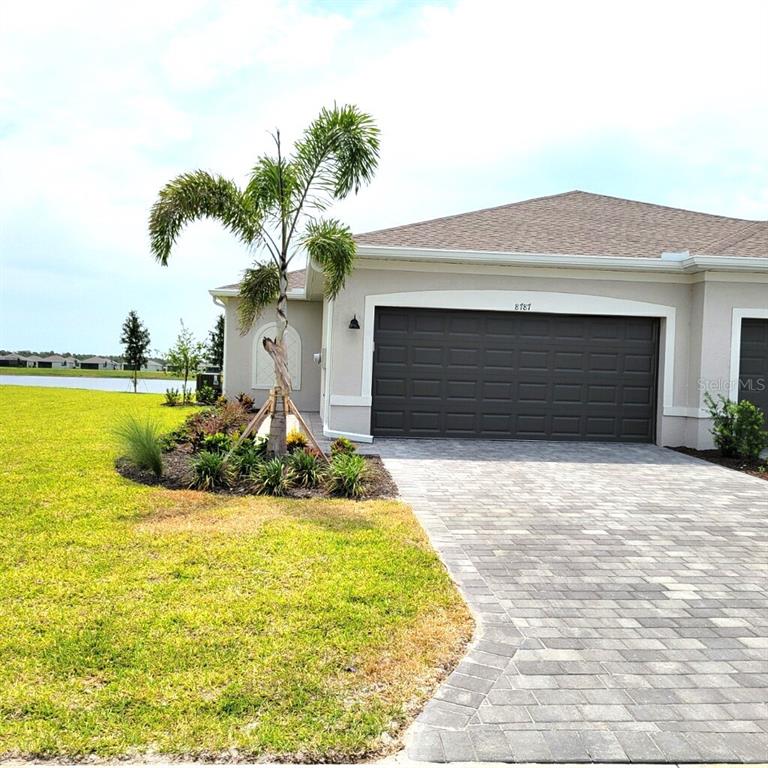 A single-story house exterior features a paved driveway, a two-car garage, and a palm tree — 8787 SAINT KITTS CIRCLE, ENGLEWOOD, FL