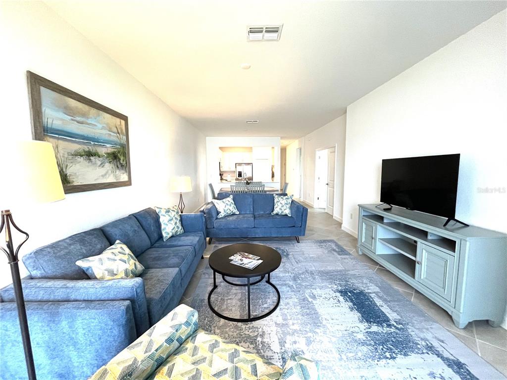 A living room features blue sofas, a round coffee table, and a television on a console — 8787 SAINT KITTS CIRCLE, ENGLEWOOD, FL