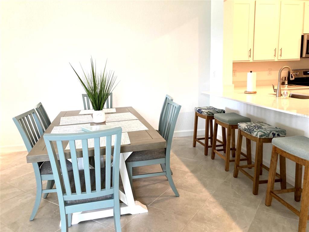 A dining area with a wooden table and blue chairs sits beside a kitchen island — 8787 SAINT KITTS CIRCLE, ENGLEWOOD, FL