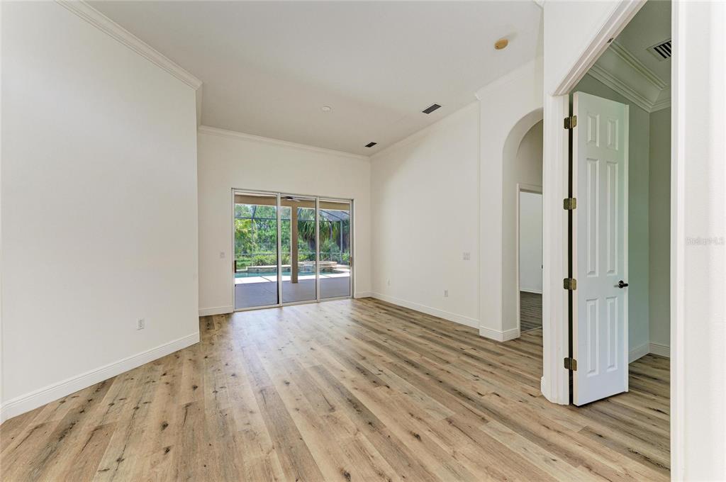 An empty room with wood-look flooring, white walls, and sliding glass doors leading to a pool — 22809 NIGHT HERON WAY, BRADENTON, FL