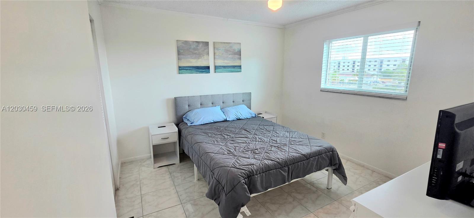 A bedroom features a gray bed, two white nightstands, tiled flooring, and a window — 2145 Pierce St # 305, Hollywood FL 33020, HOLLYWOOD, FL