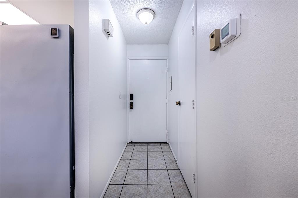 A tiled entryway features a white door, a ceiling light, and a wall-mounted thermostat — 5197 SILENT LOOP UNIT 224, NEW PORT RICHEY, FL