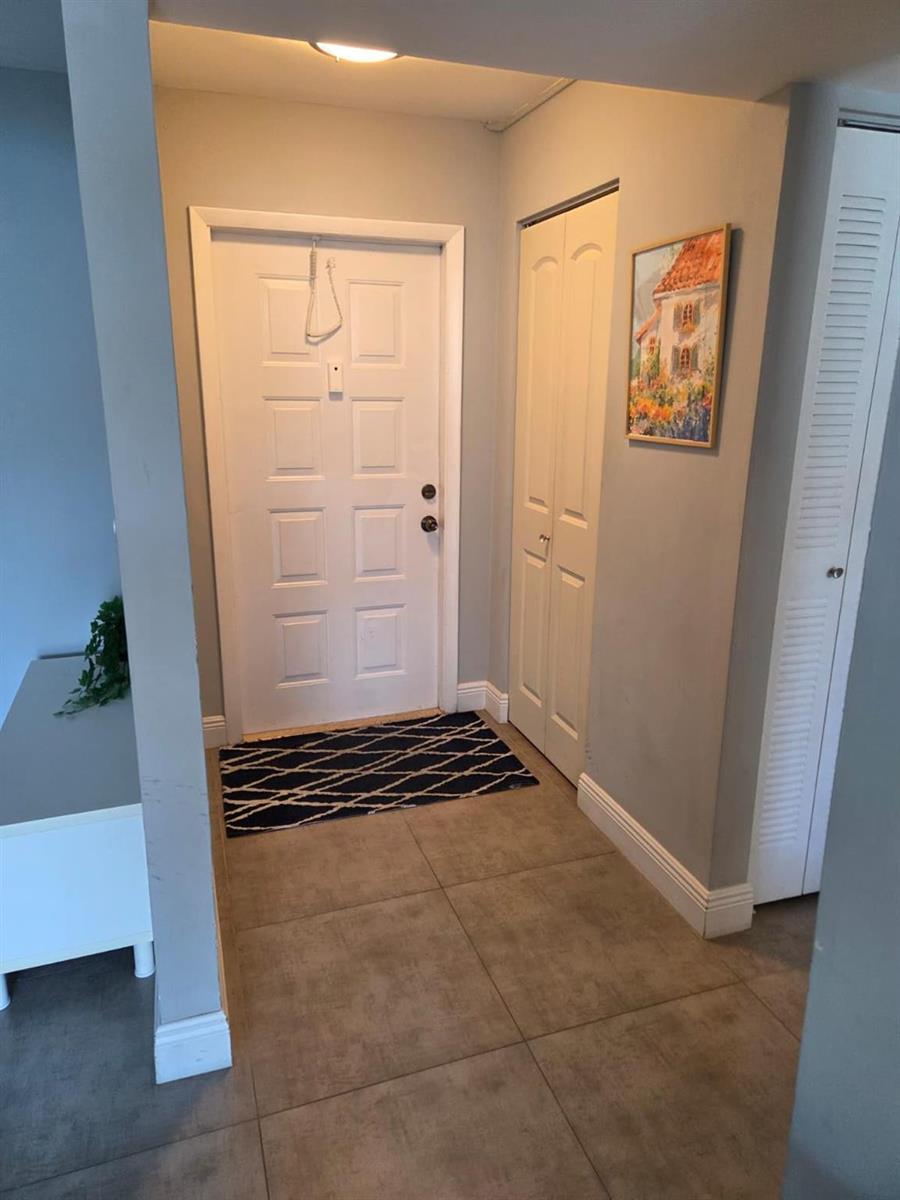 An entryway features a white front door, tiled flooring, a patterned rug, and closet doors — 3500 Blue Lake Drive # 304, Pompano Beach FL 33064, POMPANO BEACH, FL