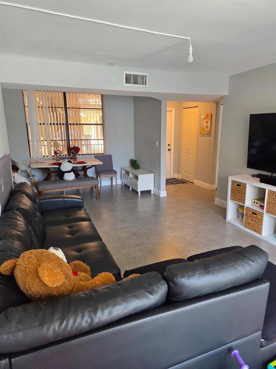 A living room with tile flooring, a black leather sectional, and an adjacent dining area — 3500 Blue Lake Drive # 304, Pompano Beach FL 33064, POMPANO BEACH, FL