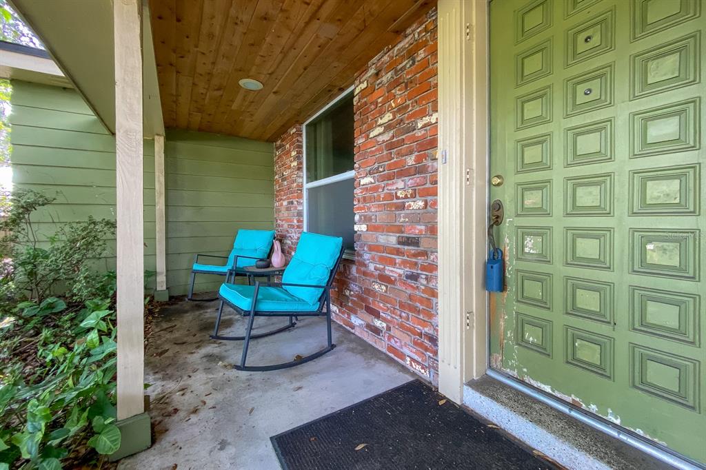 A covered front porch features a green paneled door, brick siding, and two blue rocking chairs — 810 ORANGE VIEW DRIVE, LARGO, FL
