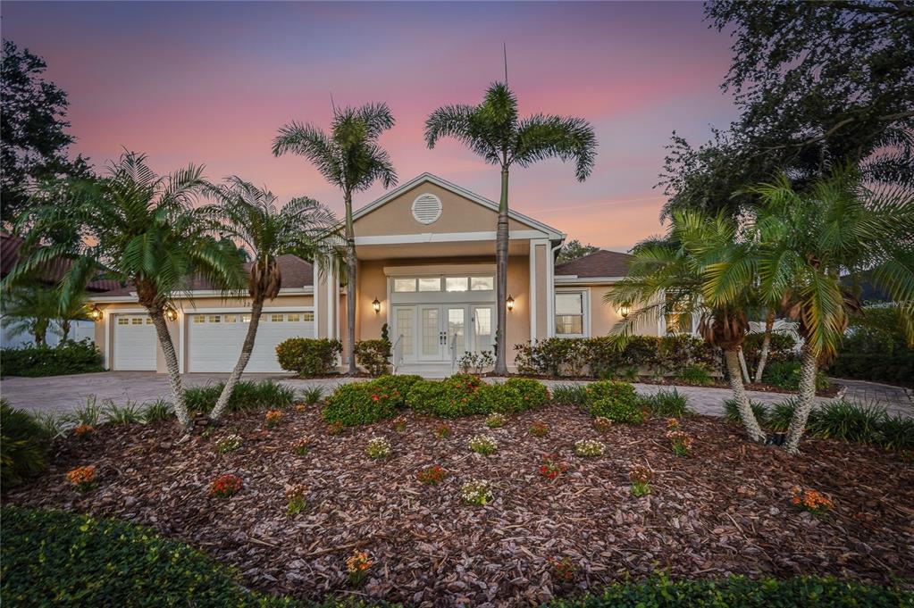 A single-story house with a beige exterior, a three-car garage, and palm trees at sunset — 121 HARBOR VIEW LANE, BELLEAIR BLUFFS, FL
