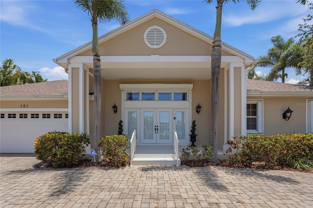 The exterior of a single-story house features a paved driveway, double front doors, and palms — 121 HARBOR VIEW LANE, BELLEAIR BLUFFS, FL