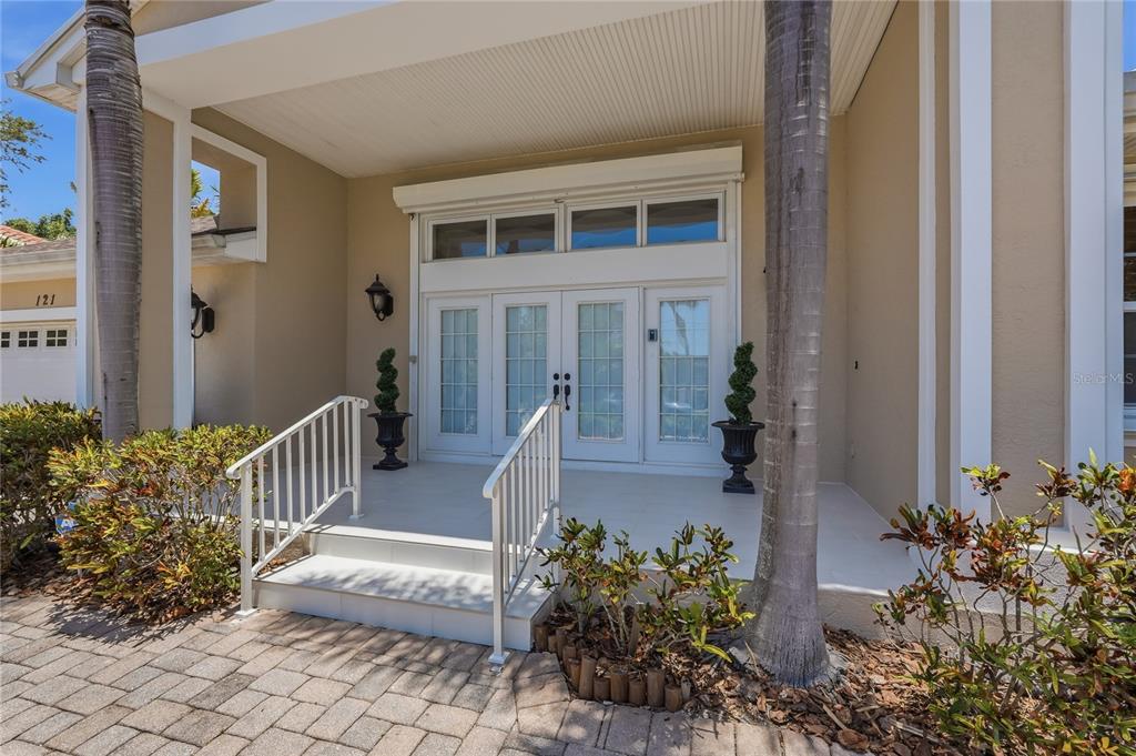 A covered front porch features white double doors, a tiled floor, and metal railings — 121 HARBOR VIEW LANE, BELLEAIR BLUFFS, FL